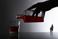 Hand pouring alcohol from a bottle into a glass with small outline of mother and child in the distance